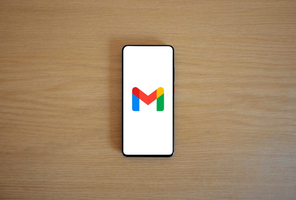 pexels photo 20716656 20716656 A smartphone displaying the Gmail app logo on a wooden surface, viewed from above.